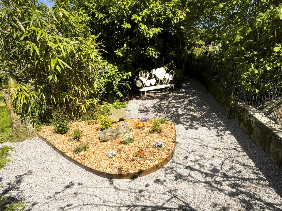 Paysage extérieur d'une maison montrant à la fois des éléments d'aménagement paysager et de maçonnerie : au premier plan une terrasse pavée ou dallée récemment construite, flanquée de massifs de plantes bien entretenus, d'arbustes taillés et de pelouse verte. L'arrière-plan peut inclure une clôture en aluminium ou un portail. La scène doit montrer clairement les deux domaines de compétence : espaces verts d'un côté et structures maçonnées de l'autre, illustrant ainsi le double savoir-faire de l'entreprise.